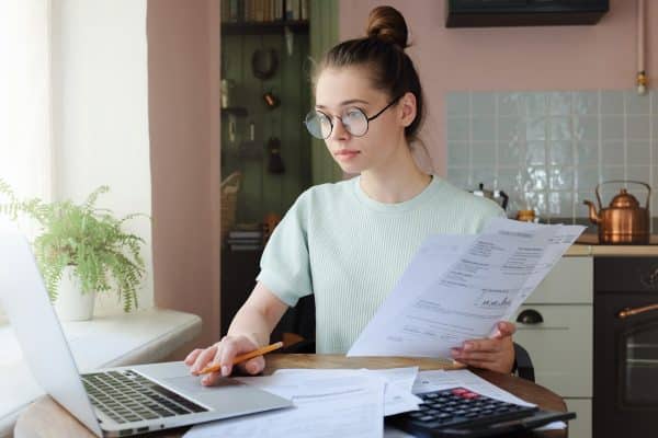 Women working behind her laptop, holding a paper in her hands